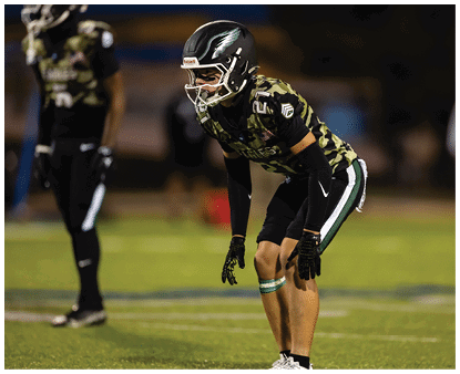 A group of people wearing camouflage-patterned football uniforms and helmets are standing together on a lit football field at night. Description generated by AI