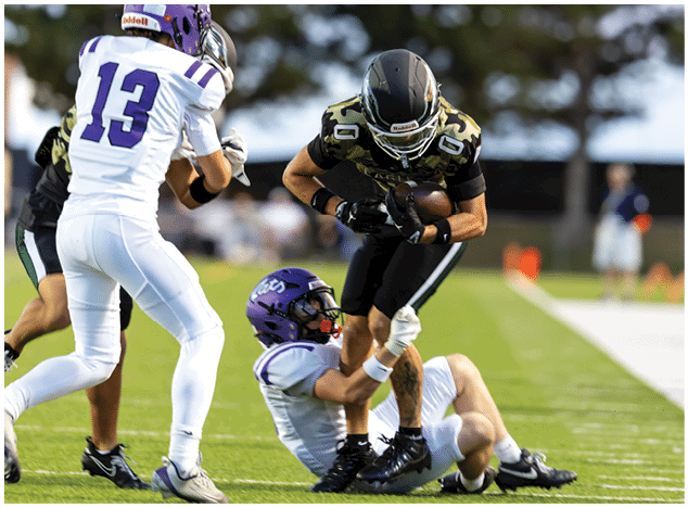People in football uniforms are lined up on a field facing each other, preparing for a play during a game. Description generated by AI