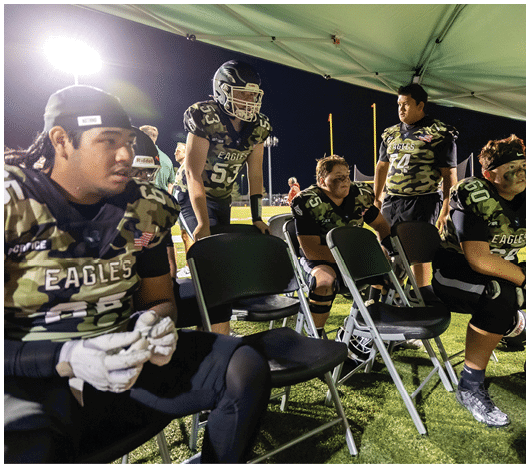 People in football uniforms are lined up on a field facing each other, preparing for a play during a game. Description generated by AI