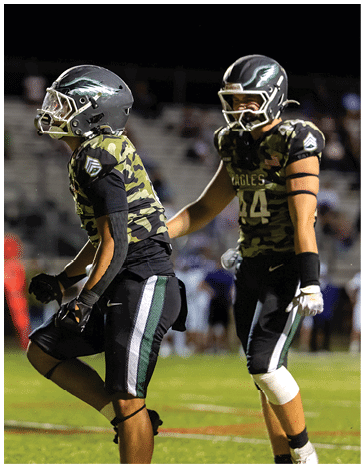 People in football uniforms are lined up on a field facing each other, preparing for a play during a game. Description generated by AI