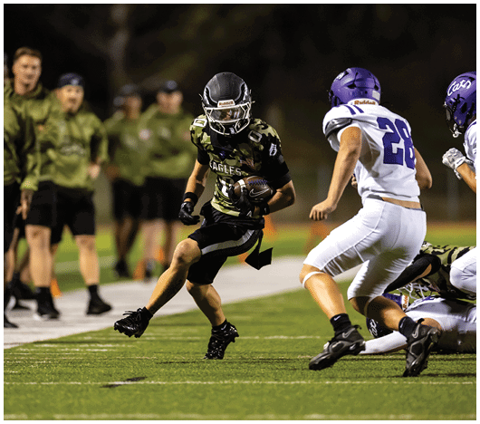 People in football uniforms are lined up on a field facing each other, preparing for a play during a game. Description generated by AI