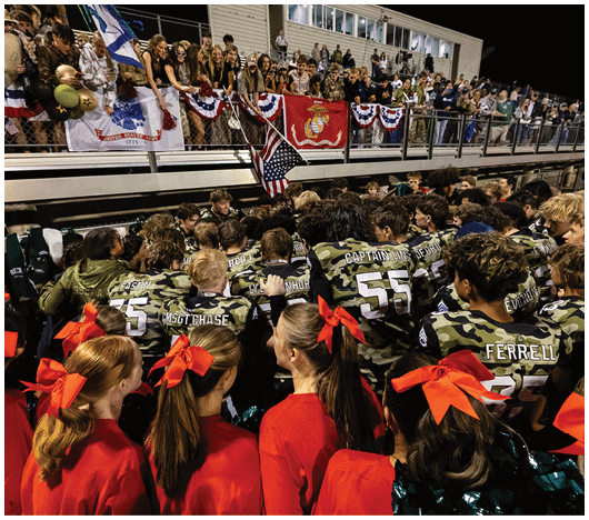 People in football uniforms are lined up on a field facing each other, preparing for a play during a game. Description generated by AI