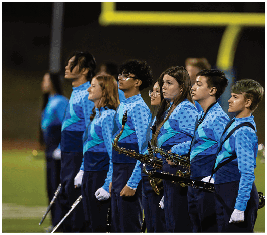People in football uniforms are lined up on a field facing each other, preparing for a play during a game. Description generated by AI