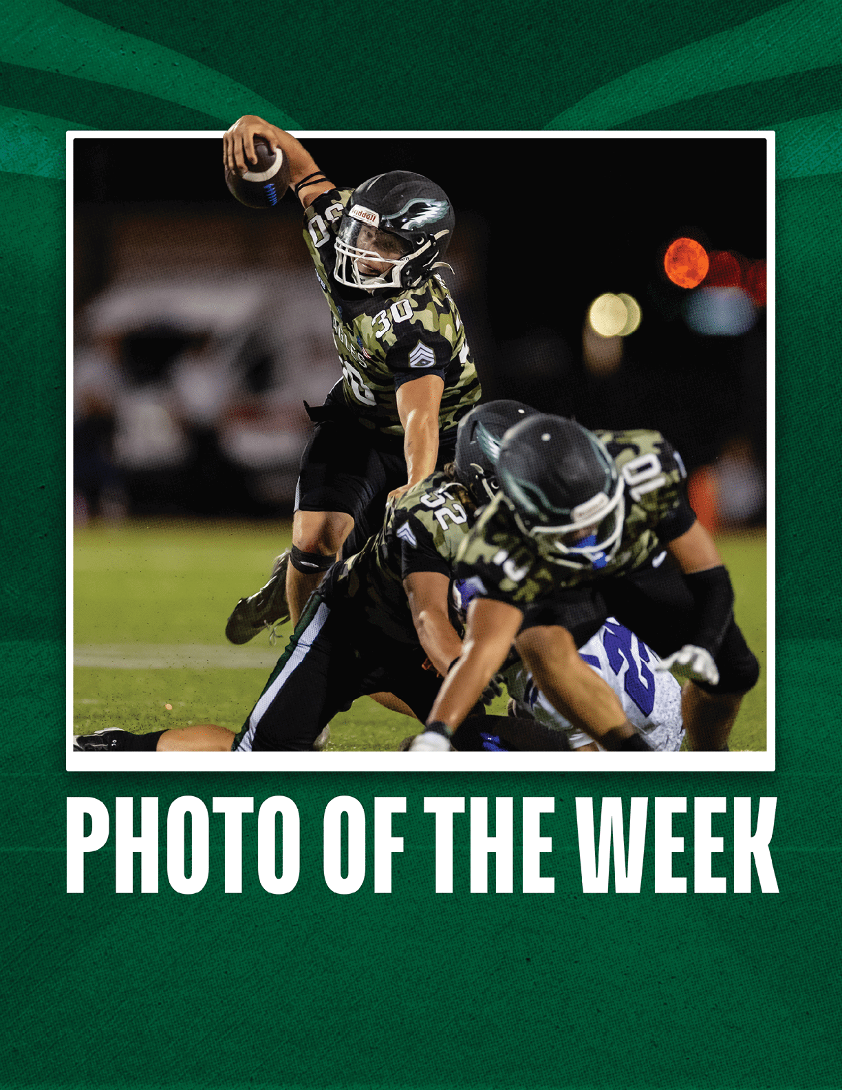 A person in a camouflage football uniform is running with the ball while another person in a similar uniform blocks an opponent on a football field at night. Description generated by AI