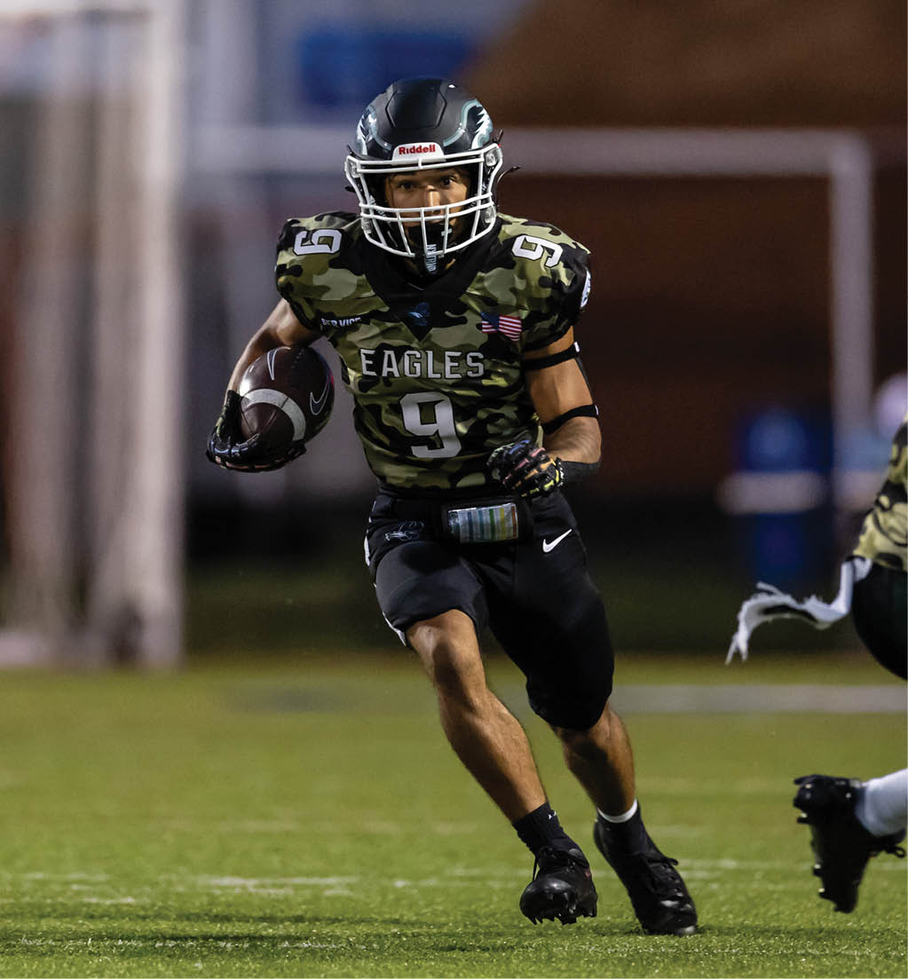 A person wearing a camouflage football jersey with the number 9 and the word Eagles is running on a field while holding a football. Description generated by AI