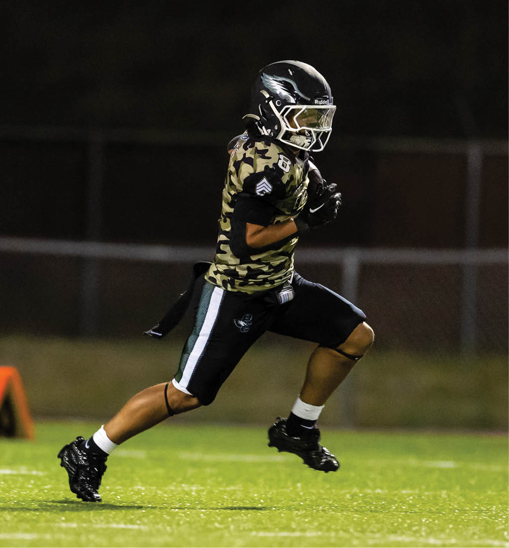 A person wearing a camouflage sports jersey and helmet is running on a grassy field at night while holding a football. Description generated by AI