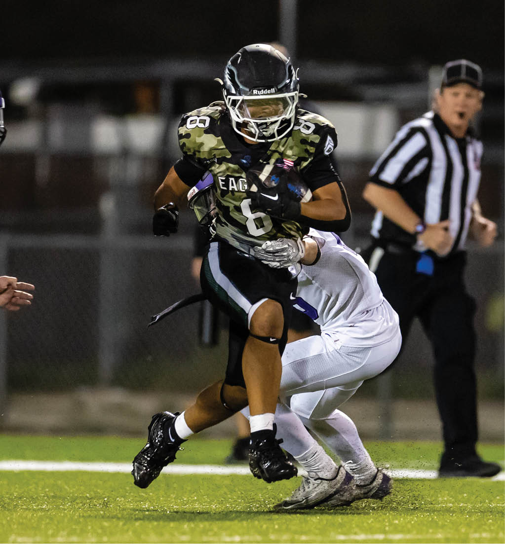 A person wearing a camouflage football uniform with the number 6 is running while another person in a white uniform attempts to tackle them on a football field with a referee and another person in the background. Description generated by AI