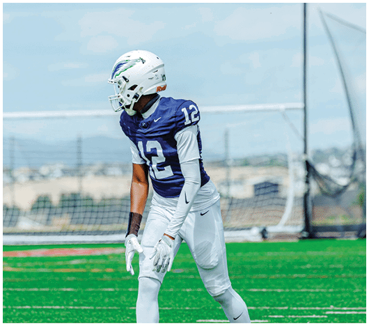 A person wearing a white football helmet and a blue jersey with the number 12 is looking to the side against a cloudy sky background. Description generated by AI