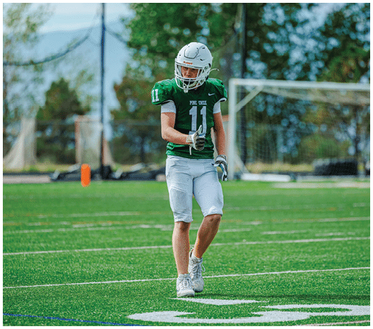 A person wearing a green football jersey with the number 11 and white helmet is standing on a green football field near a goalpost. Description generated by AI