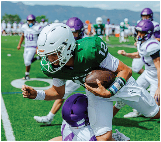 Two people in football uniforms are engaged in a tackle on a green field with white yard lines. Description generated by AI