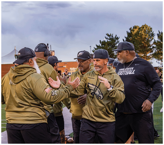 A group of people wearing sports team apparel and caps are engaged in a lively conversation or celebration outdoors near a sports field. Description generated by AI