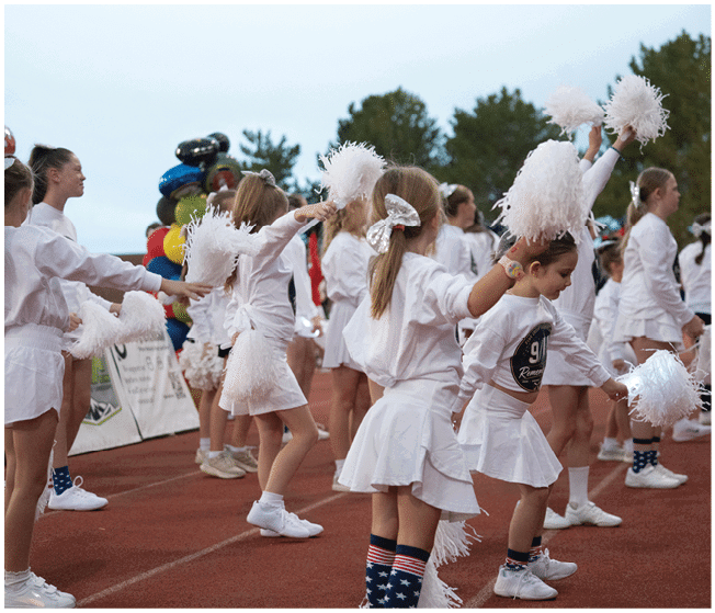 A group of people dressed in white cheerleading outfits with pom-poms are performing a routine on a track field. Description generated by AI