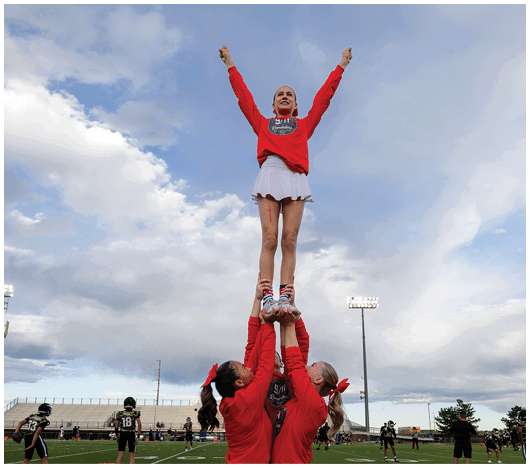 A person wearing a red sweatshirt and white skirt is standing with arms raised against a blue sky. Description generated by AI