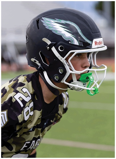 A person wearing a camouflage sports jersey with the number 28 and a black helmet with an eagle wing design is on a football field. Description generated by AI