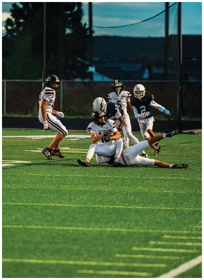 A person wearing a sports uniform and helmet is running on a green football field near the end zone at dusk. Description generated by AI