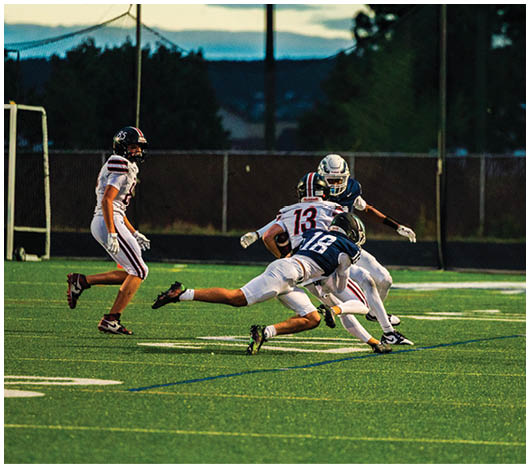 People playing football on a field at dusk with one player tackling another while others watch nearby. Description generated by AI