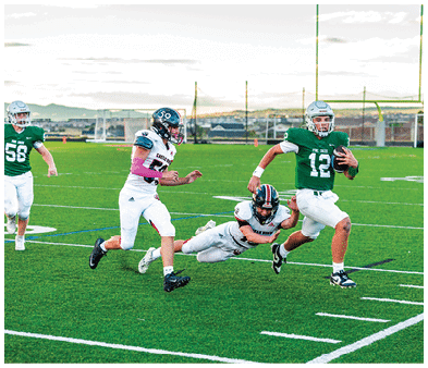 Two people wearing football uniforms are on a field with one person in a green jersey running towards the other person in a white jersey against a backdrop of mountains and a partly cloudy sky. Description generated by AI