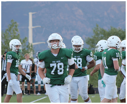 Several people wearing green and white football uniforms are standing on a field, appearing to prepare for or participate in a game. Description generated by AI