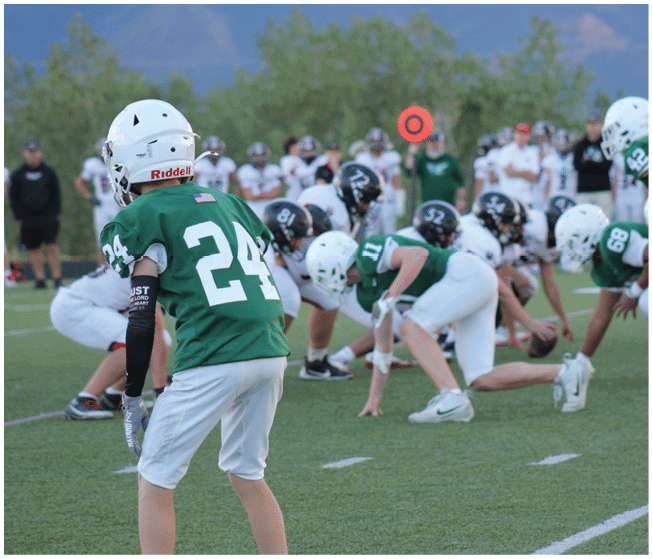 Children in football uniforms are positioned on a field preparing for a play during a game. Description generated by AI