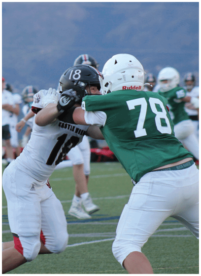 A person wearing a green sports jersey with the number 11 and white helmet is running on a football field with other players and people in the background. Description generated by AI
