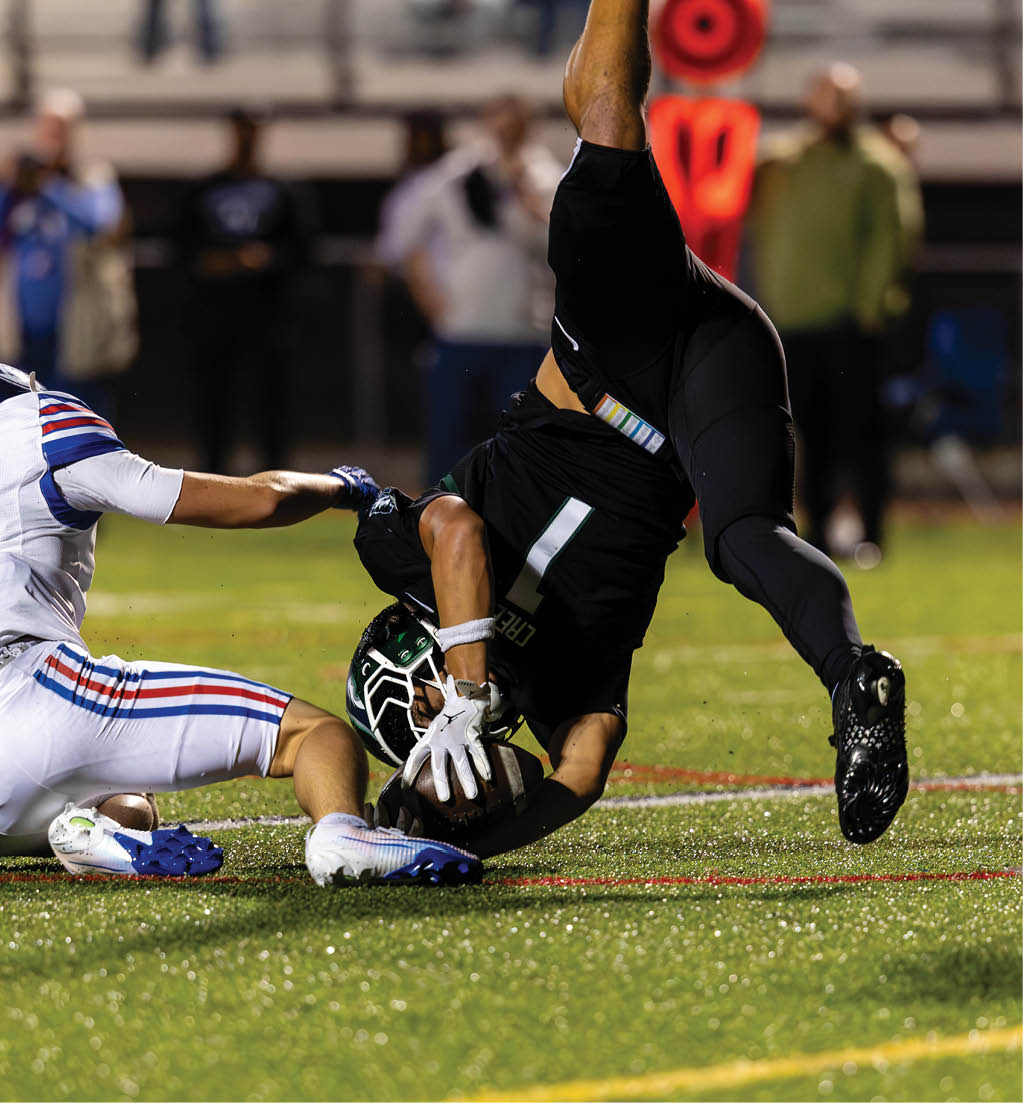 Two football players in action on a field, with one player in white tackling another player in black who is falling forward while holding the ball. Description generated by AI