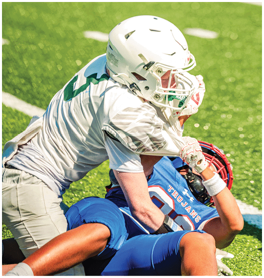 Two people in football uniforms are engaged in a tackle on a grassy field during a game. Description generated by AI