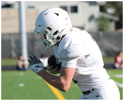 A person wearing a white football uniform and helmet is holding a football and running on a green field. Description generated by AI