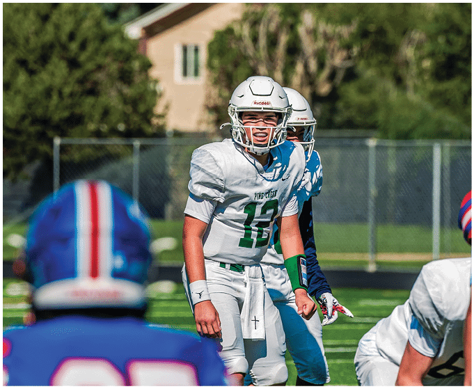 Two people wearing football uniforms are on a field with one person in a green jersey running towards the other person in a white jersey against a backdrop of mountains and a partly cloudy sky. Description generated by AI