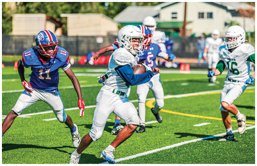 Two people wearing football uniforms are on a field with one person in a green jersey running towards the other person in a white jersey against a backdrop of mountains and a partly cloudy sky. Description generated by AI