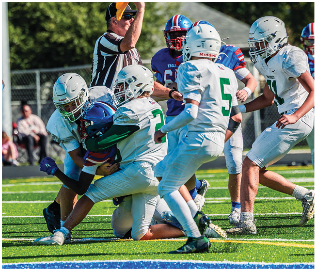 Two people wearing football uniforms are on a field with one person in a green jersey running towards the other person in a white jersey against a backdrop of mountains and a partly cloudy sky. Description generated by AI