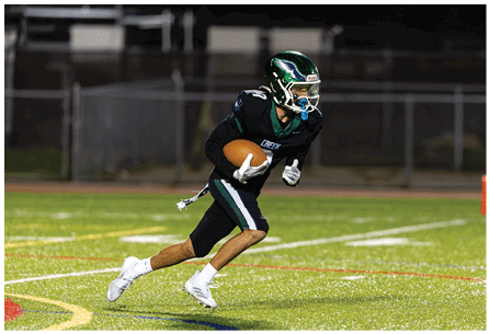 A person wearing a black football uniform and helmet is running on a field while holding a football. Description generated by AI
