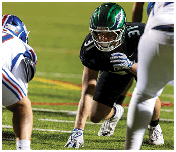 Two people in football uniforms are positioned on a field facing each other, preparing for a play. Description generated by AI