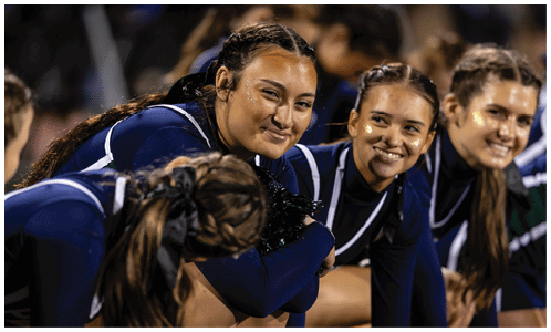 A group of people in matching dark blue athletic uniforms are sitting closely together, smiling and appearing engaged in a shared moment. Description generated by AI