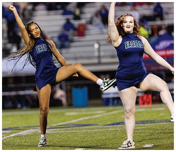 Two adults in blue cheerleading uniforms with “EAGLES" on the front are performing a coordinated dance routine on a football field. Description generated by AI