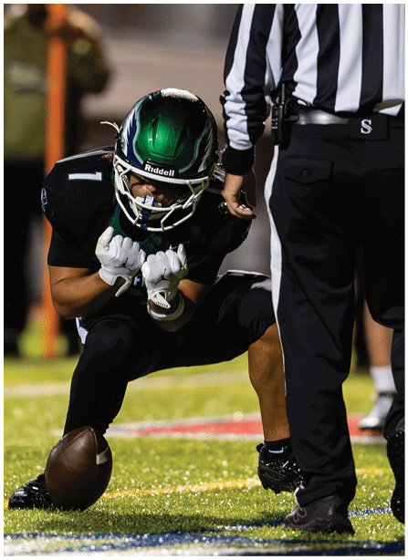 A person in a football uniform is crouched down preparing to snap the ball while a referee stands nearby on a football field. Description generated by AI
