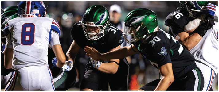People in football uniforms are actively engaged in a game, with one person holding the ball and others preparing to block or tackle. Description generated by AI
