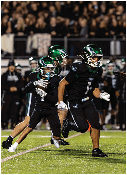 Three people in black football uniforms and green helmets are actively playing on a field, with one person holding a football and another running ahead. Description generated by AI