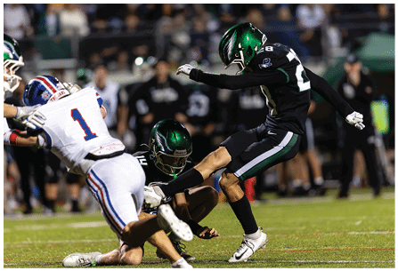 Two people in black football uniforms with green helmets are tackling a person in a white football uniform with the number one on the back during a game on a grass field. Description generated by AI