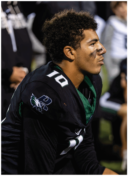 A person wearing a dark sports jersey with the number 10 is shown in close-up from the side, focusing on their curly hair and ear. Description generated by AI