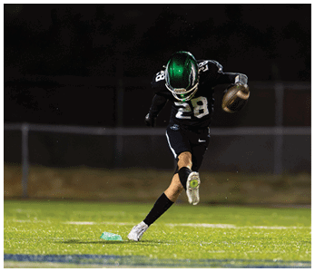 A person wearing a black sports uniform with the number 28 is kicking a football on a grassy field at night. Description generated by AI