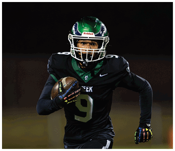 A person wearing a green and black football uniform with the number nine is running while holding a football during a nighttime game. Description generated by AI