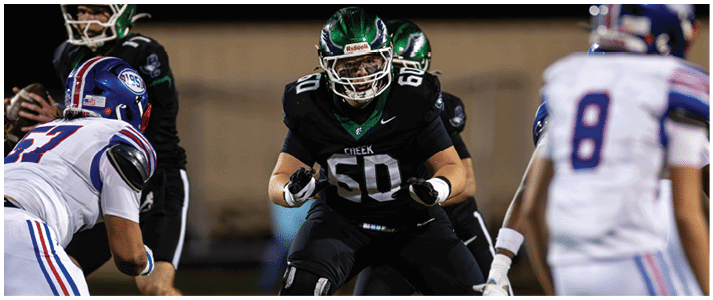 A group of people in football uniforms are positioned on a field, with one person in a black uniform crouched and ready to engage with others in white uniforms. Description generated by AI