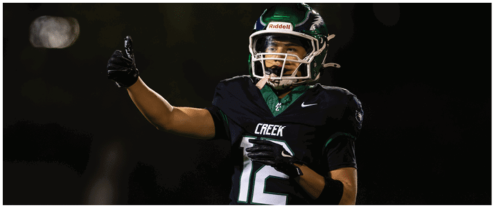 A person wearing a black football uniform with the number 12 and the word “CREEK" is giving a thumbs-up gesture on a dark field. Description generated by AI