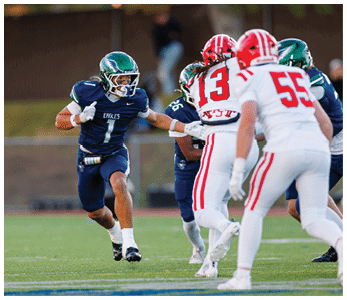 A person in a blue football uniform with the number one is running on a field while two people in white and red football uniforms with numbers thirteen and fifty-five are positioned in front of them. Description generated by AI