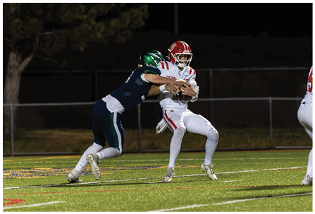 Two people in football uniforms are engaged in a tackle on a grassy field during a nighttime game. Description generated by AI