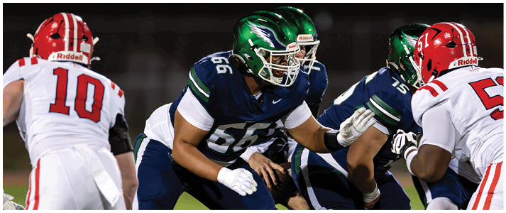 People in football uniforms are positioned on a field preparing for a play during a game. Description generated by AI