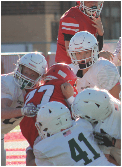 Several people wearing football helmets and uniforms are engaged in a close physical play on a football field. Description generated by AI