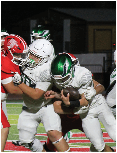 Two people wearing football helmets and uniforms are engaged in a close physical play during a nighttime game. Description generated by AI