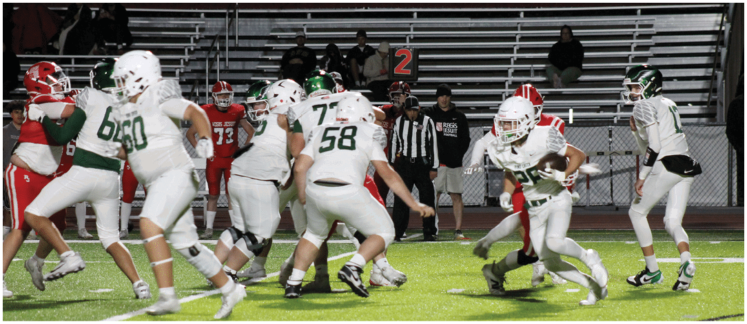 People wearing football uniforms are actively playing on a green field under stadium lights. Description generated by AI