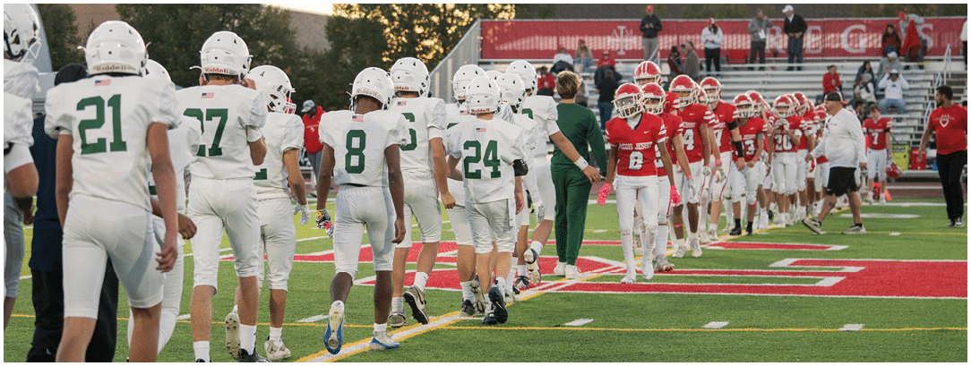 Two teams of people in football uniforms are lined up on a field shaking hands after a game during sunset. Description generated by AI